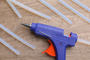Dark blue glue gun and sticks on wooden table, flat lay