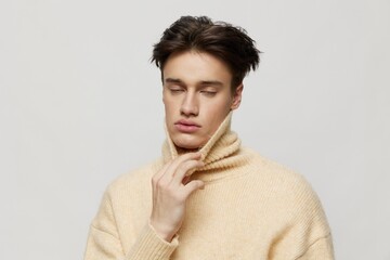 a handsome young man with dark short curly hair combed back in a beige jumper with a high collar...