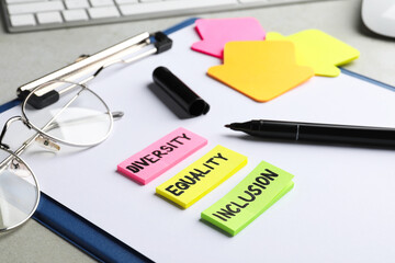 Sticky notes with words Diversity, Equality, Inclusion, marker and glasses on grey table, closeup