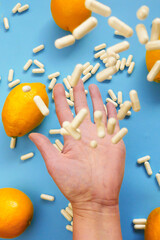 Taking vitamin C tablets.White capsules of vitamin C in a hand and yellow lemon citrus fruits on a blue background.Tablets fly into the hand.View from above.Health and medicine concept. 