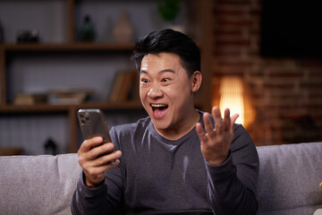 Asian Man celebrating mobile success by showing yes gesture. Excited asian man getting great news,...