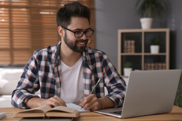 Young man watching webinar at table in room