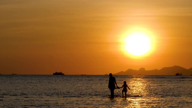 Female and child little girl silhouette on Sunset on water surface. Friendship, love and happy family forever on summer vacation