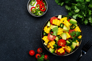 Tex-mex spicy salad with corn, avocado, jalapeno peppers, cherry tomatoes and cilantro. Black stone kitchen table background, top view, copy space
