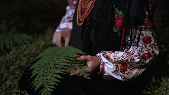 Witch woman in traditional ukrainian costume collects herbs, ferns at night in Carpathian mountains forest. National dress - vyshyvanka, ancient coral beads. Folk medicine concept.