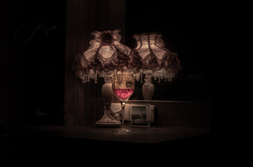 Fototapeta na wymiar A glass of red wine in the dim light of Vintage lamp with reflection from mirror. Light and Shadow, Dark tone, Copy space, Selective focus.