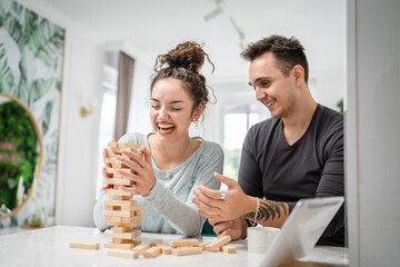 young couple woman and man play jenga game at home on the table