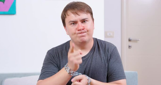 Man hands are chained with metal chain, he turns his head and threatens revenge with gestures, take revenge. Domestic violence man in hopeless state bound by circumstances promises retribution