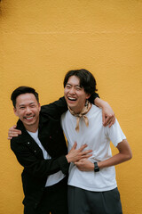 黄色い背景の前で、笑顔で寄り添う同性カップル