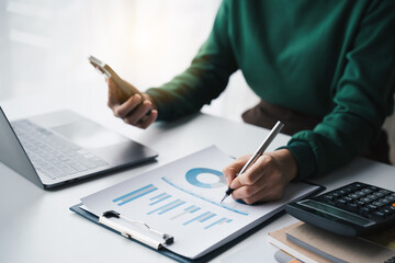 hand of business woman hold smartphone use analyzing and calculating the annual income and expenses, a financial chart and financial report, technology and bussiness concept.