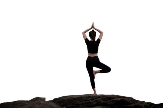 The back of a woman wearing sportswear doing a yoga pose on the rocks.