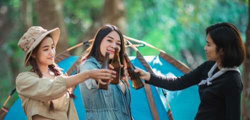 Young women cheer and drink beverage  front of camping tent
