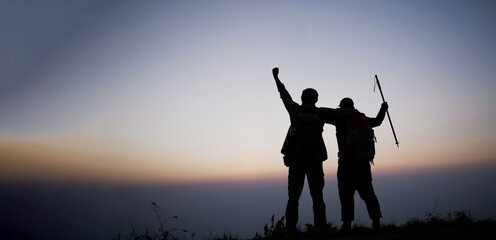 Fototapeta na wymiar Silhouette of cheering hiking men open arms to the sunrise stand on mountain