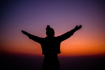 Fototapeta na wymiar Silhouette of cheering hiking woman open arms to the sunrise stand on mountain