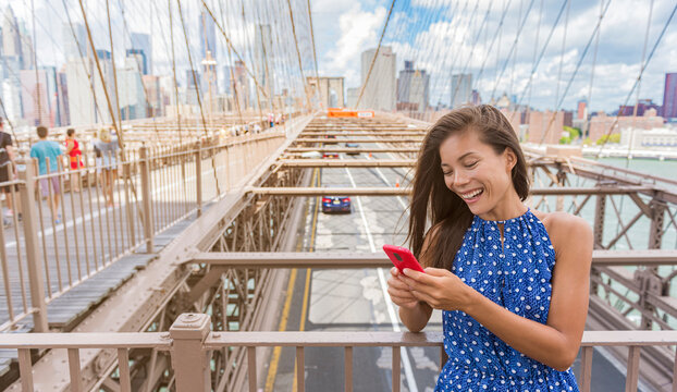 New York woman using phone app walking on Brooklyn Bridge towards Manhattan city skyline. Young female professional multicultural lady, New York City, USA