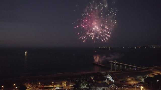 imagen aérea desde un dron de show pirotécnico. fuegos artificiales en el mar con explosiones y colores. Show lanzado desde muelle de pescadores. Se ve la ciudad iluminada de fondo
