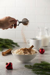 Sprinkle cinnamon over Scandinavian rice porridge in a bowl surrounded by Christmas balls. Breakfast on New Year's Eve.