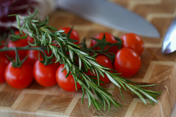 Organic cherry tomatoes with rosemary on wooden board with knife