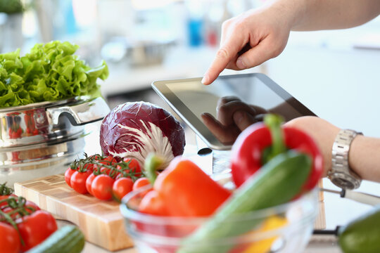 Person holding digital tablet and fresh vegetables in kitchen