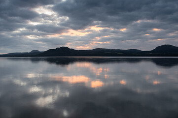 光が見える暗い雲に覆われた空を湖面に反射する湖。北海道の屈斜路湖。