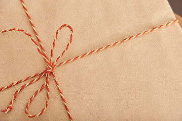 Top view of a Christmas gift wrapped in neutral paper and tied with a red and gold decorative string. Simple close up image with copy space.