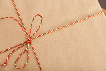 Top view of a Christmas gift wrapped in neutral paper and tied with a red and gold decorative...