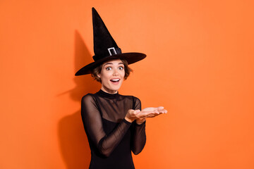 Photo of cute excited lady wear black witch dress cap holding arms empty space isolated orange color background