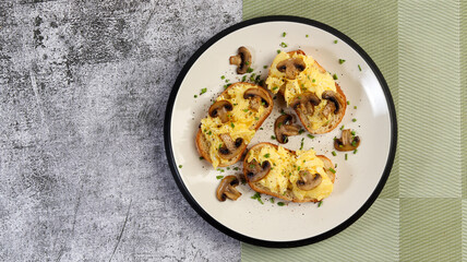 Scrambled eggs with champignons mushrooms on toast on a round plate on a dark gray background. Top view, flat lay