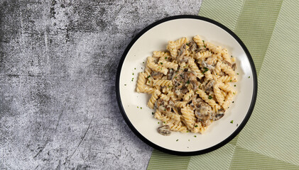 Creamy pasta with champignon mushrooms on a round plate on a dark gray background. Top view, flat lay