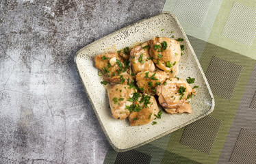 Oven Baked Garlic Chicken thighs with herbs on a square  plate on a dark background. Top view, flat lay