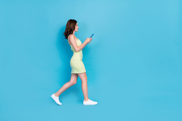 Obraz premium Full length photo of pretty cute girl dressed green clothes walking typing modern device empty space isolated blue color background