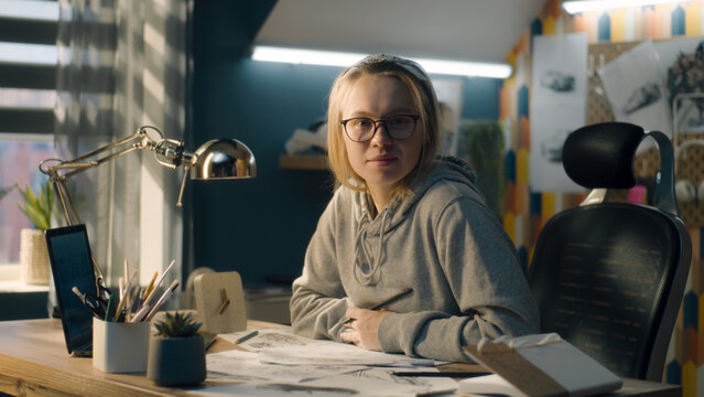 Creative designer in a home based design studio stops sketching and looks at the camera smiling. Pencil sketches, storyboard, video editing, story telling.