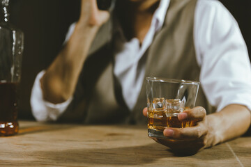 Close-up shot of a man using smartphone while drink of whiskey alcoholic beverage at bar counter in the pub.