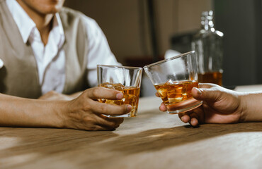 A close-up shot of two men clinking whiskey glasses together while at the bar counter in a pub.