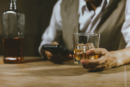 Close-up shot of a man using smartphone while drink of whiskey alcoholic beverage at bar counter in the pub.