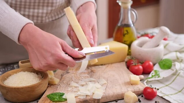 woman slicing piece of parmesan hard cheese at domestic kitchen