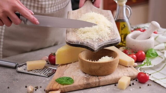 Woman pours grated parmesan cheese from wooden board into bowl