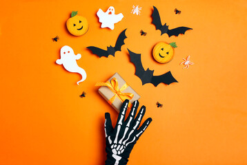 Female hand in funny spooky glove with a gift and Halloween decorations on orange background.