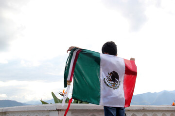 Latin Mexican boy of 8 years shows the flag of Mexico proud of his culture and tradition celebrates...
