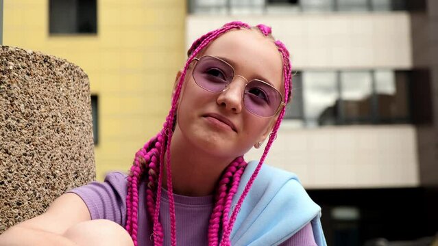 Portrait of a smiling caucasian teenage girl with pink braids and with braces on her teeth on a street background.Summer concept.Generation Z style.Selective focus,close-up.