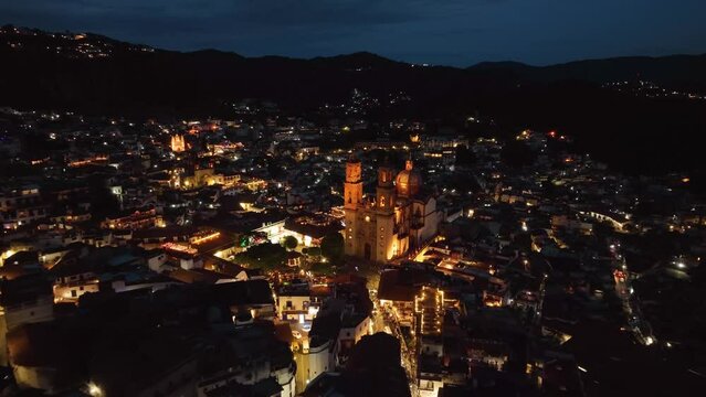 Aerial view overlooking the illuminated cityscape of Taxco Guerrero approaching the church, night in Mexico