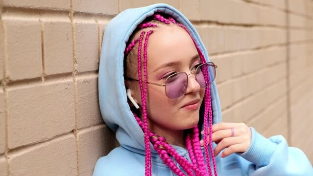 Portrait of a caucasian teenage hipster girl with pink braids against a pink brick wall.Generation Z style.