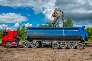 Process of loading scrap metal into truck using hydraulic grab loader. Work outdoors.