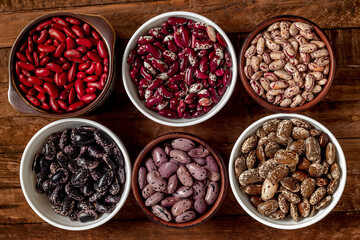 Ceramic bowls with different organic beans on a wooden background. Scarlet runner, kidney, anasazi, pinto beans. Top view.
