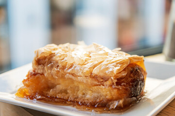 Delicious Greek sweet pastry named Galaktoboureko, made of semolina custard in filo, served with honey in white plate.