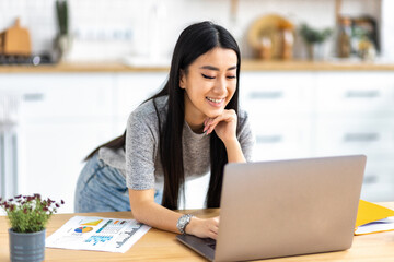 Smiling Asian woman working online remotely at home using laptop computer. Distant work