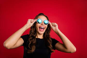 Photo of cool impressed young lady dressed black t-shirt arms dark glasses smiling open mouth isolated red color background
