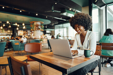 Smiling young african woman sitting with laptop in cafe - Powered by Adobe