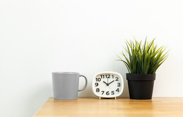 Small white alarm clock, black numbers, set the time for 10.10 o'clock, placed on a wood table.