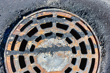 A cast-iron storm sewer hatch on the road before laying the asphalt pavement poured with bitumen. Drainage of rainwater from the road surface. Close-up.